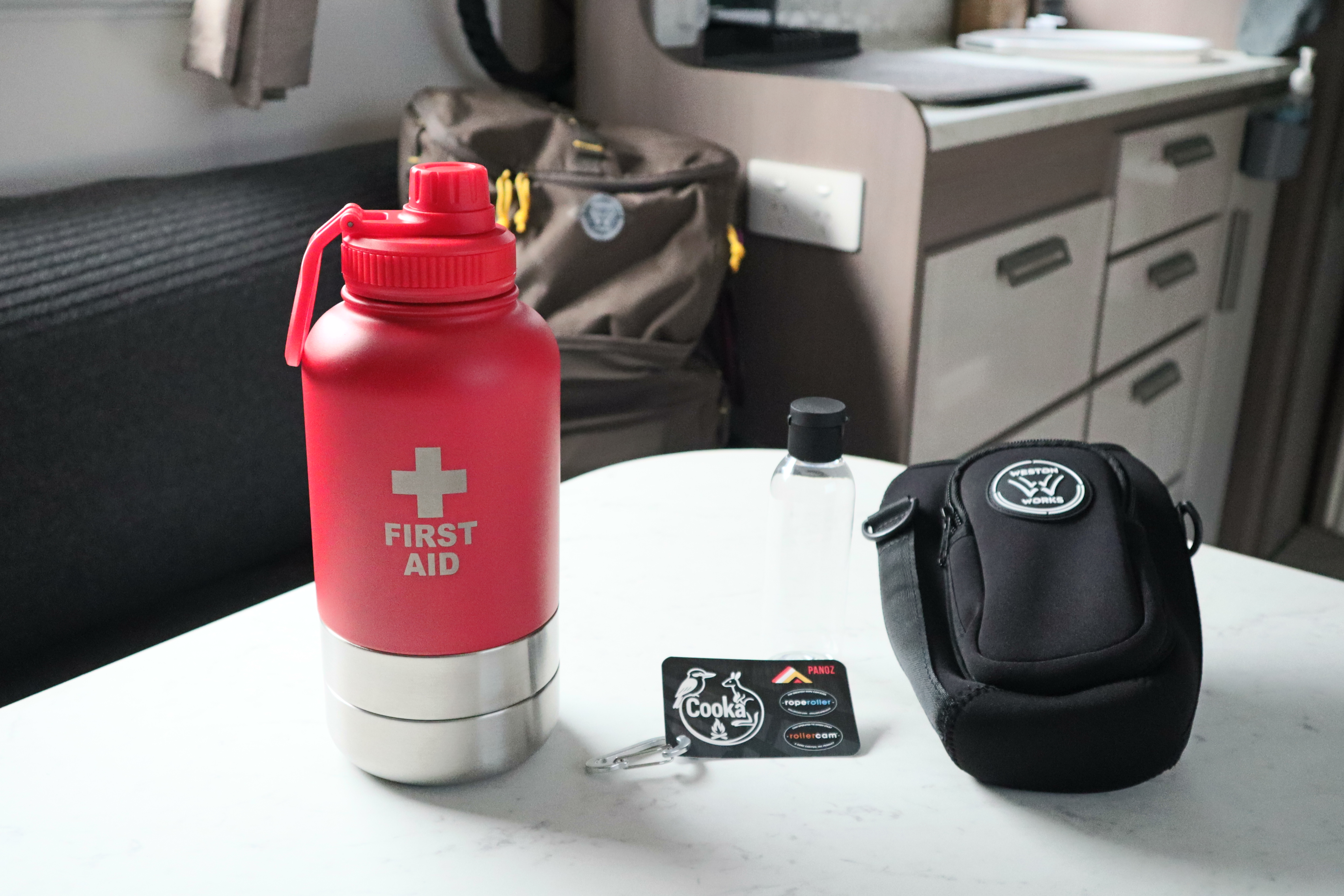 Assembled red WestonWorks First Aid Bottle next to a small travel bottle and empty carry pouch