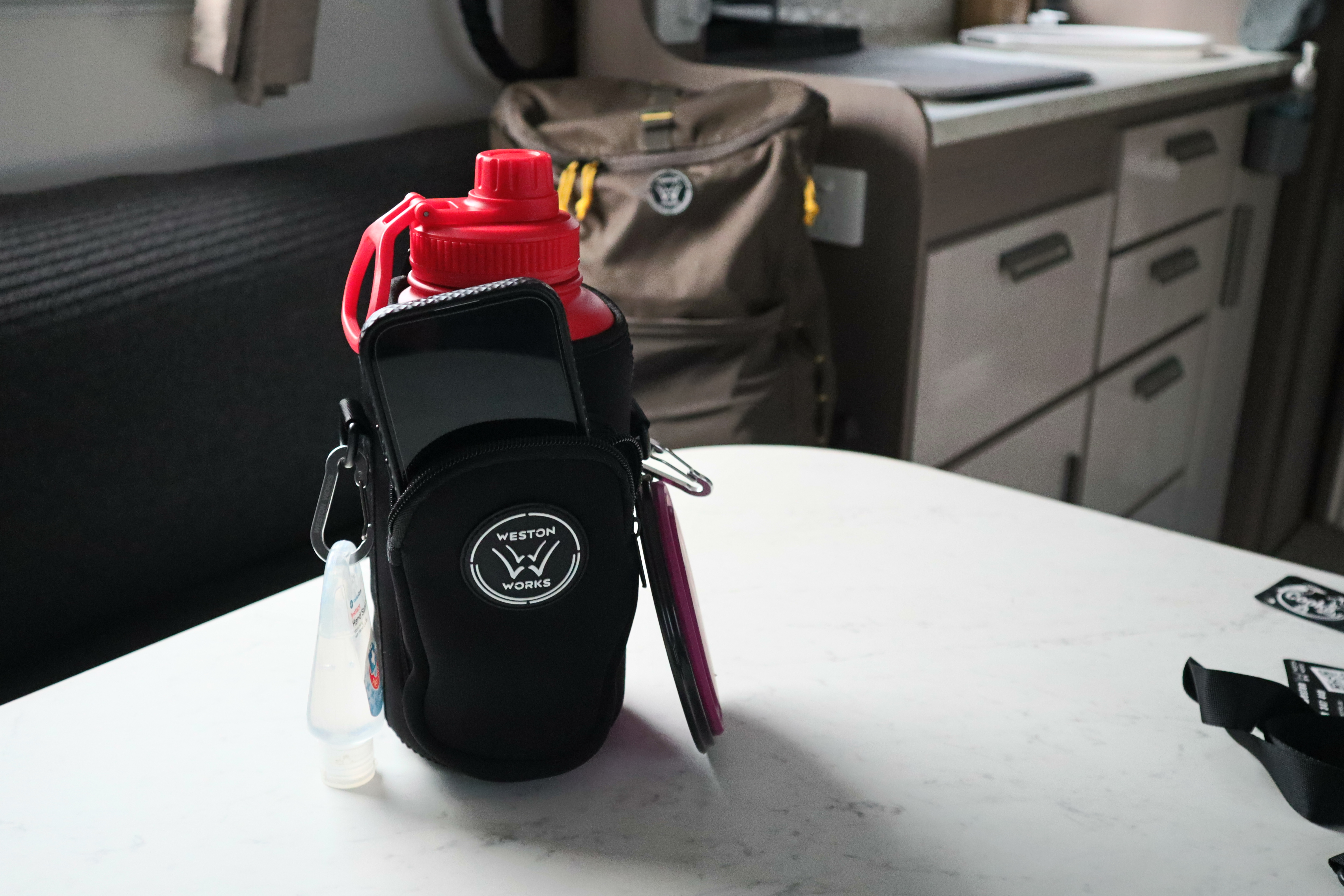 WestonWorks First Aid Bottle in its carry pouch with a phone in the front zip pocket