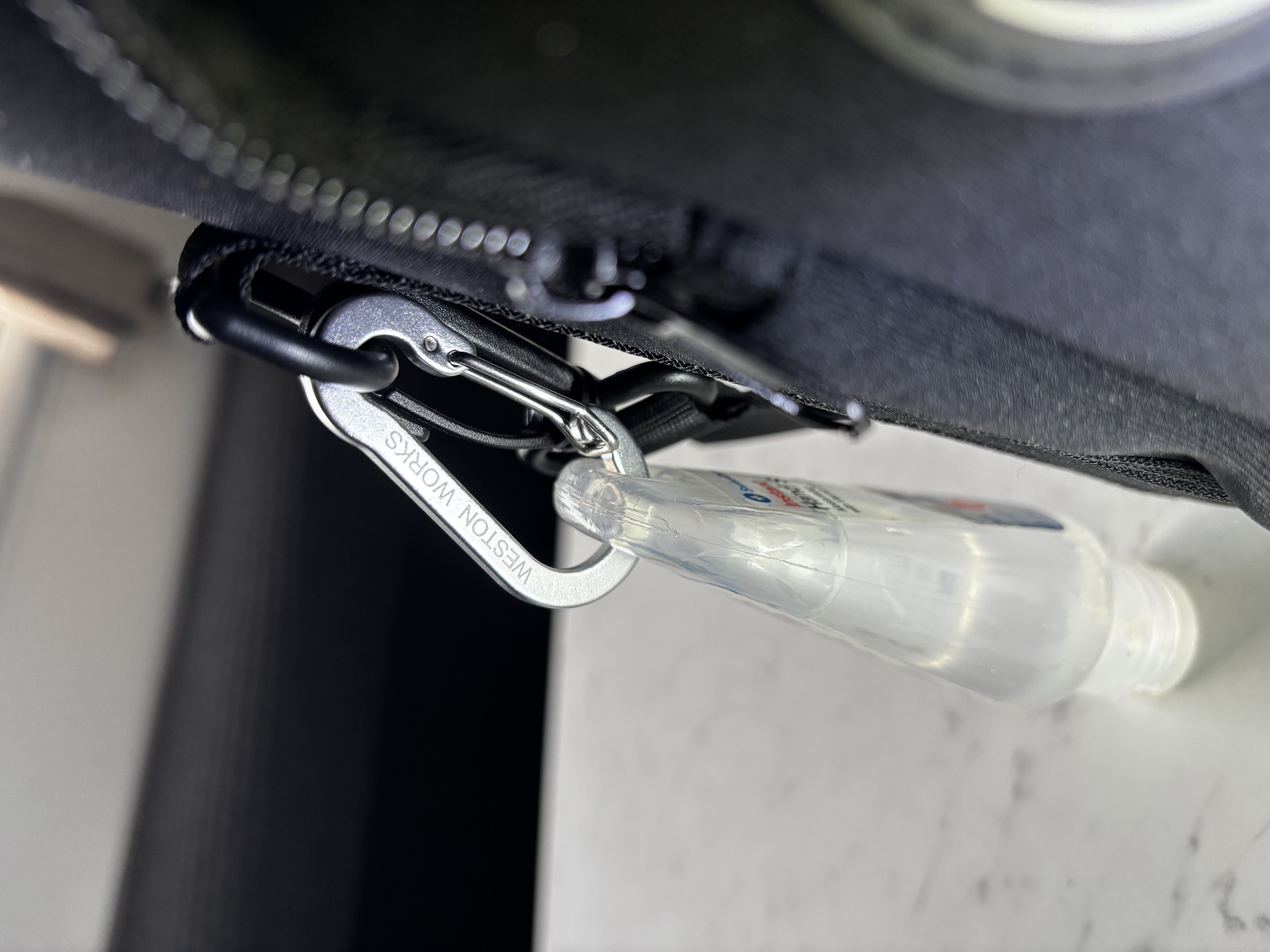 Close-up of a WestonWorks branded carabiner clip holding a hand sanitiser bottle